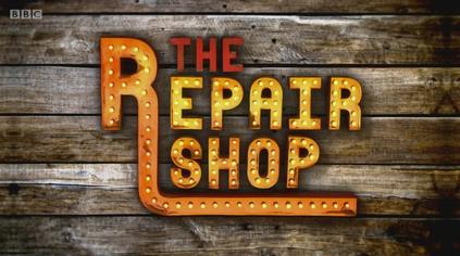 Wooden Wall with lettered sign reading "The Repair Shop" picked out in lights.